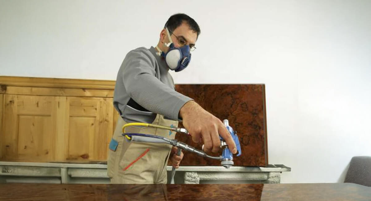 Lakierobejca - jak wybrać idealny pistolet natryskowy do drewna i mebli istolet natryskowy aplikujący lakierobejcę na drewnianą powierzchnię, ukazując równomierne krycie