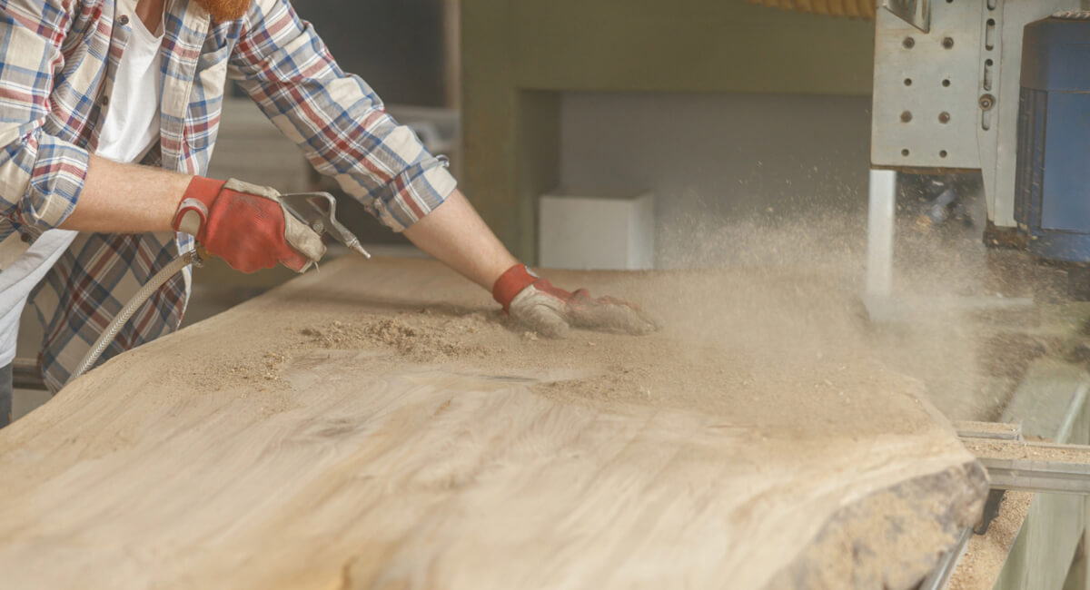 Pracownik stolarni oczyszczający powierzchnię z trocin za pomocą pistoletu na sprężone powietrze