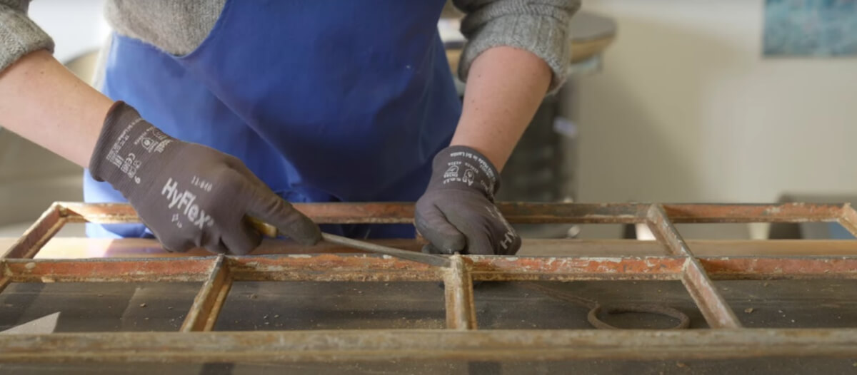 Zbliżenie na narożnik ramy, gdzie śrubokręt pomaga usunąć resztki rdzy